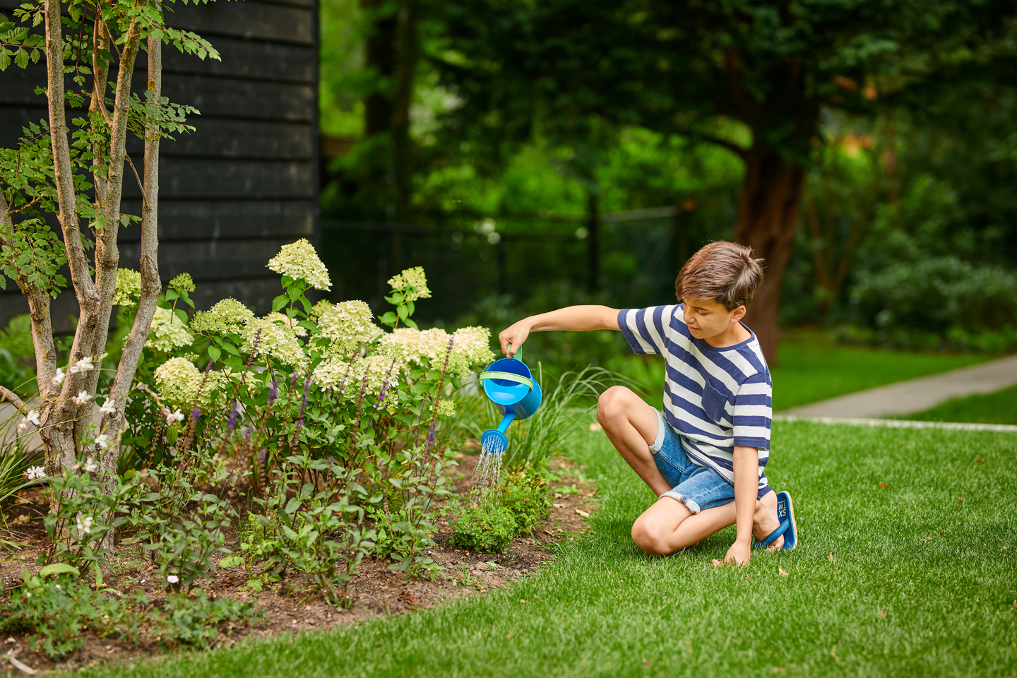 jongen geeft met gieter de planten in de tuin water