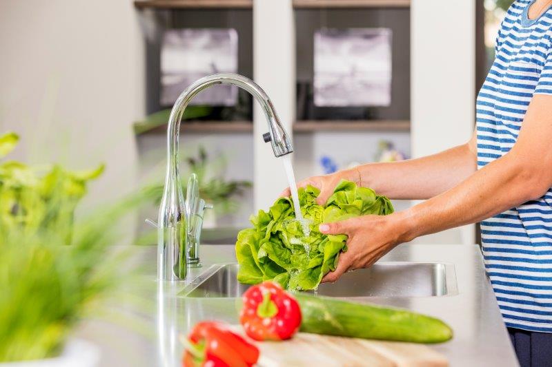 Vrouw wast groente onder waterstraal