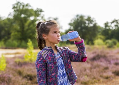 Meisje met blauwe waterbidon buiten in de natuur