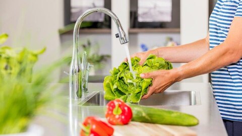 Vrouw wast groente onder waterstraal