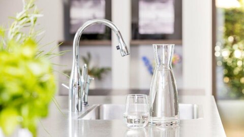 Glas water en karaf bij keukenkraan