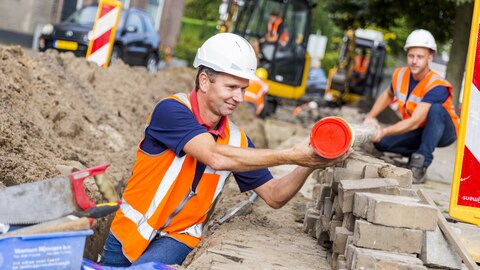 Man werkt aan leidingwerk in gleuf op straat