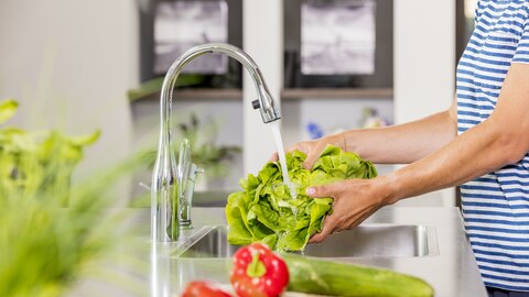 Vrouw wast groente onder waterstraal